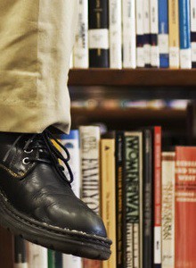 Man Reading Book and Sitting on Bookshelf in Library --- Image by © Royalty-Free/Corbis